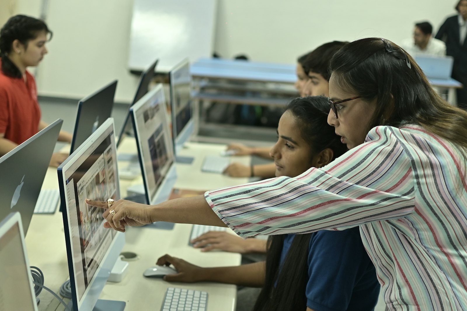 Instructor guiding students at computers in a college computer lab
